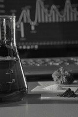 Chemical laboratory. Graphs on the computer, a flask with a chemical composition and reagents on the table. Black and white photo of scientific research in the field of biology or chemistry.