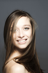 Naklejka premium brunette girl turning head with flowing hair in the air studio portrait against gray background..