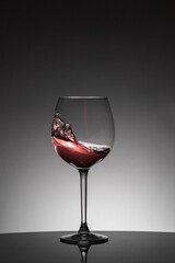 Moving red wine inside a glass. Back lighting, studio shot.