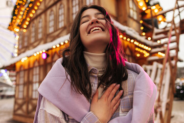 Obraz premium Close-up of positive young caucasian woman laughing with closed eyes spends leisure time outside. Brunette wears shirt and sweater. Concept of positive emotions, good mood.