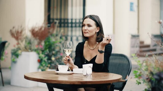 Beautiful brunette woman sitting on outdoor terrace. Caucasian female drinking champagne in the restautant. Slylish lady in bistro.