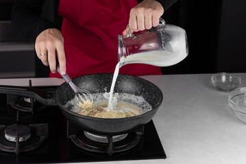 Chef cook making white cheese sauce for mac and cheese meal. Ingredients: Milk, cheese, flour and butter in wok pan on kitchen gas stove.
