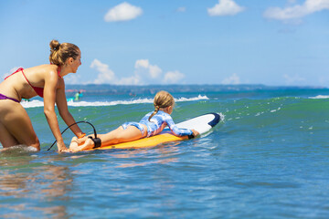 Happy baby girl - young surfer ride on surfboard with fun on sea waves. Active family lifestyle,...