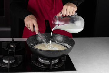 Chef cook making white cheese sauce for mac and cheese meal. Ingredients: Milk, cheese, flour and butter in wok pan on kitchen gas stove.
