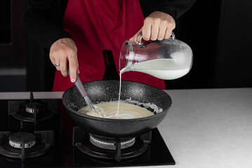Chef cook making white cheese sauce for mac and cheese meal. Ingredients: Milk, cheese, flour and butter in wok pan on kitchen gas stove.