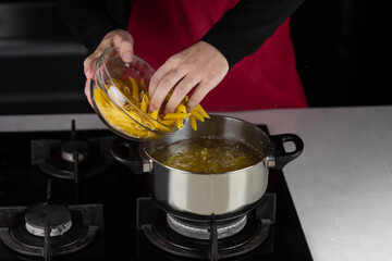 Chef cook makes macaroni pasta in boiling water on kitchen gas stove in pot.