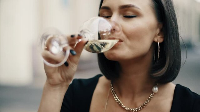Beautiful brunette woman sitting on outdoor terrace. Caucasian female drinking champagne in the restautant. Slylish lady in bistro.