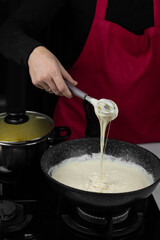 Chef cook making white cheese sauce for mac and cheese meal. Ingredients: Milk, cheese, flour and butter in wok pan on kitchen gas stove.