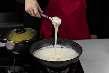 Chef cook making white cheese sauce for mac and cheese meal. Ingredients: Milk, cheese, flour and butter in wok pan on kitchen gas stove.