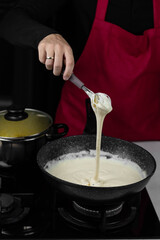 Chef cook making white cheese sauce for mac and cheese meal. Ingredients: Milk, cheese, flour and butter in wok pan on kitchen gas stove.