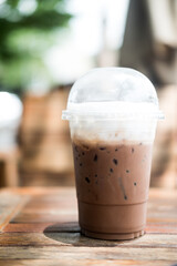 Iced mocha in transparent plastic glass on table with blurred background.