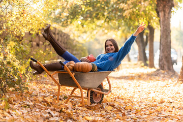 Woman have fun, lying in the garden wheelbarrow with pumpkins
