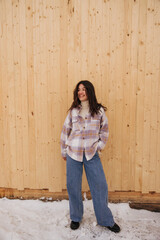 In full growth young caucasian girl loks away smiling with teeth stands on snow outside. Brunette wears jeans, golf and shirt. Concept of leisure time, winter.