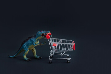 Toy dinosaur carries an empty shopping cart to the opening of store sales. Black Friday concept....