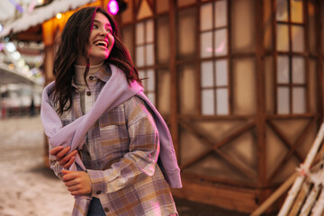 Nice young caucasian woman laughing looking away spends time at amusement park. Brunette wears shirt and sweater. Concept of positive emotions.