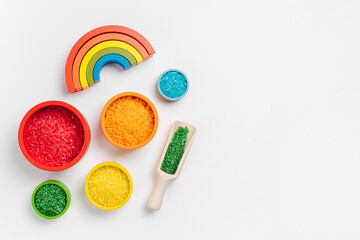 Bowls in rainbow colors with colored rice and scoops. Sensory bin toddler. Montessori material. Learning colors. Scooping and pouring activity for kids. Games for learning and development of child