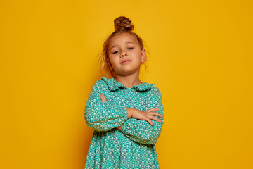 Partial image of serious little girl looking at camera. Portrait of beautiful caucasian female child wearing color dress. Childhood concept. Isolated on yellow studio background. Copy space