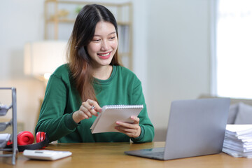 Beautiful Asian woman working on laptop and documents in home office.