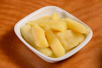 Manioc. Small portion of cooked cassava in white bowl on wooden table.