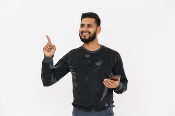 Fototapeta premium Young indian man pointing finger upward and using cellphone