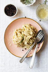 Creamy vegetarian tagliatelle Pasta with truffles and Parmigiano grated cheese served on a table with white linen, fresh rosemary, pepper, and white wine, top view close up