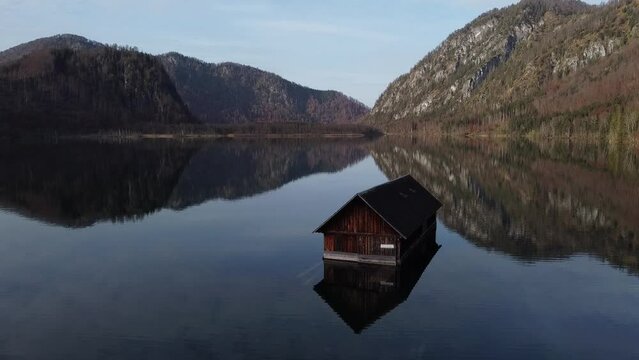 old boat house on a calm lake "Almsee" with mountains - drone footage