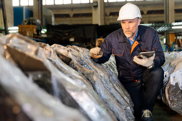 A machine factory engineer is inspecting the machines in the factory with a tablet or laptop and with a deliberate eye check. The factory is big and old.