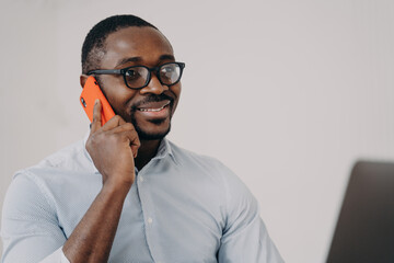 Modern african american businessman manager in glasses answers phone business call working at laptop