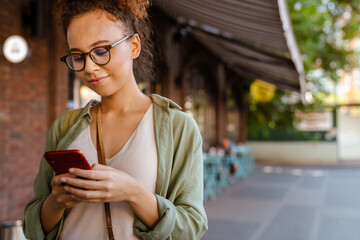 Hispanic woman in eyeglasses smiling and using mobile phone