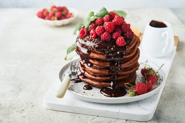 Chocolate Pancakes. Pancakes with fresh raspberry with chocolate glaze or toppings in gray bowl on light gray table background. Homemade classic american pancakes. Page for magazine concept.
