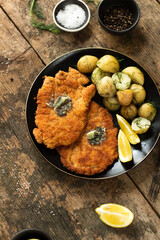 Traditional Iceland herb butter fried veal with potato wedges  on a rustic wooden table with some lemon slices and salt on the sides