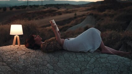 Student studies with a book on a rock at sunset