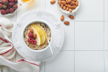 Oatmeal. Bowl of oatmeal porridge with raspberry, pear and honey on gray concrete old table background. Hot and healthy food for Breakfast, top view, flat lay