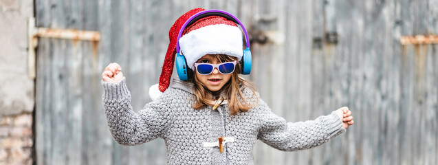 Horizontal banner or header with funny little girl wearing Santa Claus hat and sunglasses dancing...