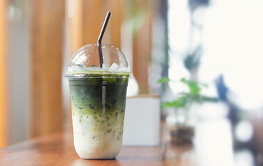 Iced green tea with milk in plastic cup on wooden table in a coffee shop.