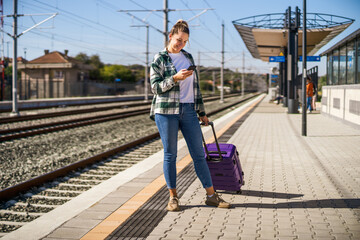 Happy woman using mobile phone on a train station.