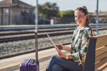 Happy woman using digital tablet while waiting for her train on a railroad station.