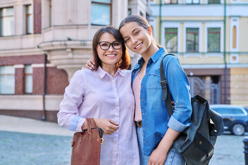 Portrait of happy mom and teenage daughter looking at camera outdoor on city street