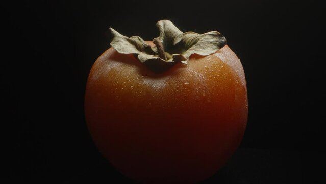 I put a wet persimmon in drops of water on the table. Black background, slow motion
