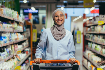 Portrait of happy woman in hijab, happy shopper in supermarket with shopping basket smiling and looking at camera