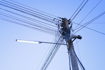 Fototapeta premium Light bulbs and power poles with confusing wires, horn loudspeakers, line announcers.