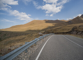 Asphalt highway in the mountains in autumn against the background of hills with grass and blue sky, autumn day in the mountains