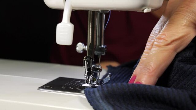 Moving sewing machine needle. Woman's hands with fuchsia-painted nails move the dark blue fabric. close up.