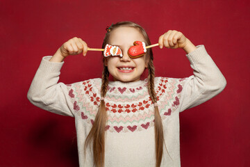 Happy funny laughing child girl with Xmas decoration gingerbread food on red background