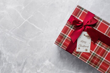 A red gift box in a cage and a label with the inscription merry Christmas on a gray marble background. Christmas holidays 2023. Buying and preparing gifts for family and relatives.