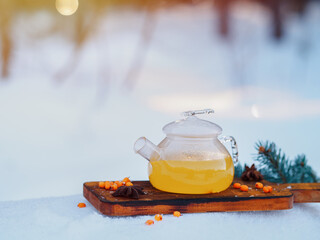Glass teapot with sea buckthorn tea in the winter forest