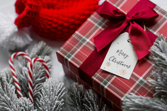 A red gift box, spruce branches, candy cane and a label with the inscription merry Christmas on a gray marble background. Christmas holidays 2023. Buying and preparing gifts for family and relatives.