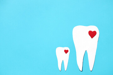Silhouettes of a large tooth and a small one with red hearts on a blue background. Flat lay, place for text.