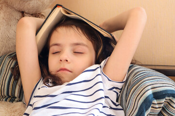 the girl is holding a book in her hands, the textbook is lying on her head, the child is tired of studying and sleeping