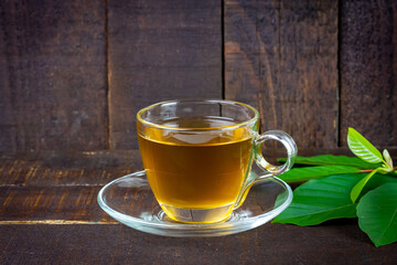 Mitragyna Speciosa Korth or kratom tea in transparent cup wtih green leaf on rustic wooden...